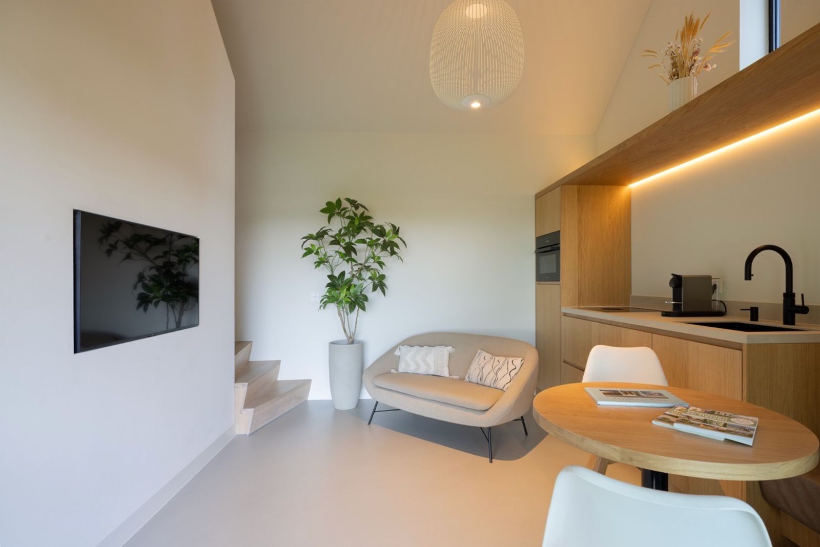 The living space of the guesthouse: oak kitchen with warm backlight, round oak dining table and cream sofa.