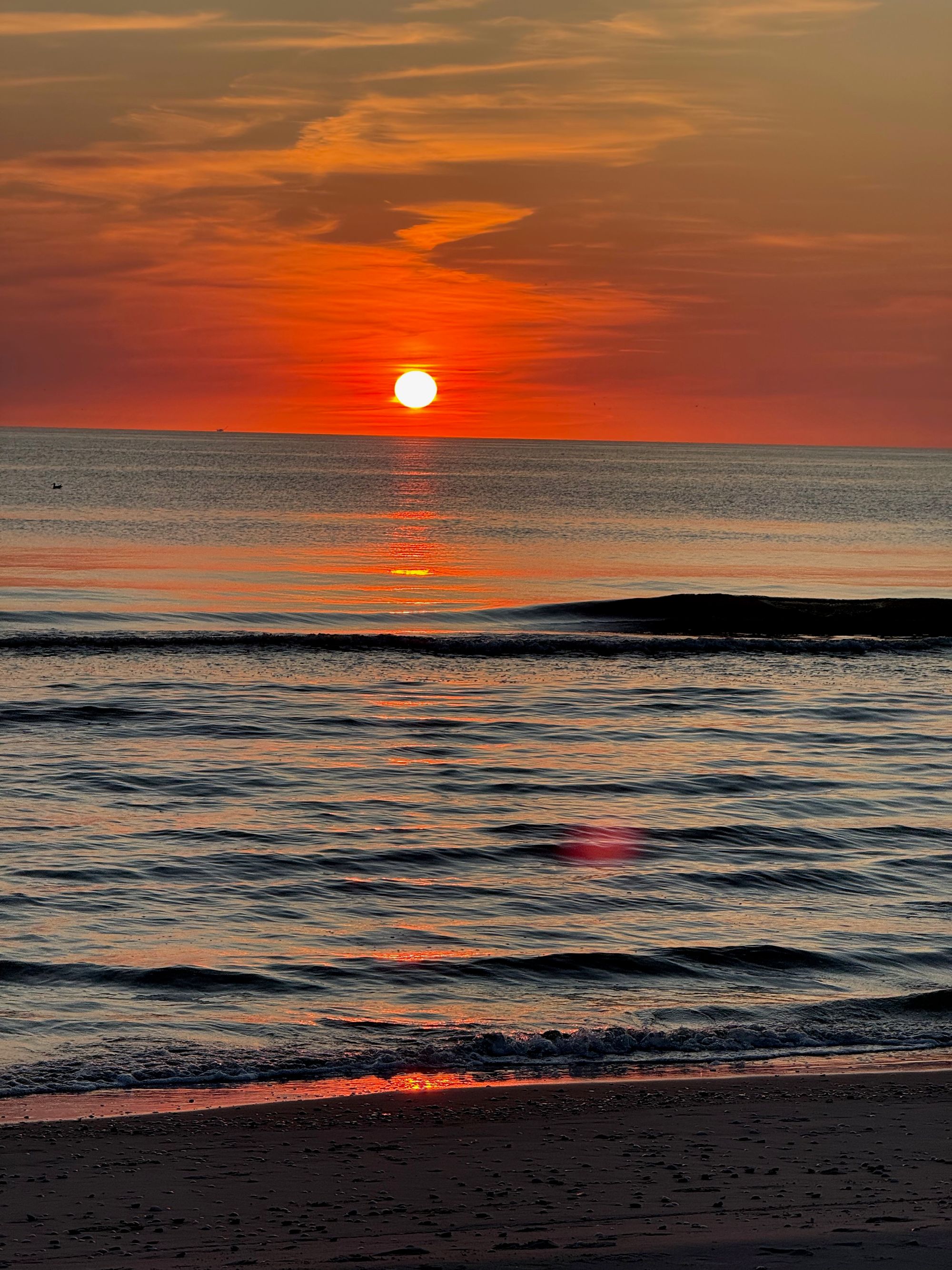 The sun setting into the sea at Bergen aan Zee, waves catching the last orange light.