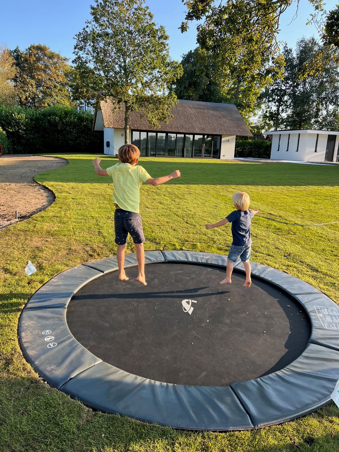 Children jumping on the in-ground trampoline in the garden, the guesthouse in the background.